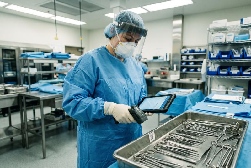 Surgical sterile processing technician scanning implant documentation and UDI label affixed to surgical tray with tablet computer